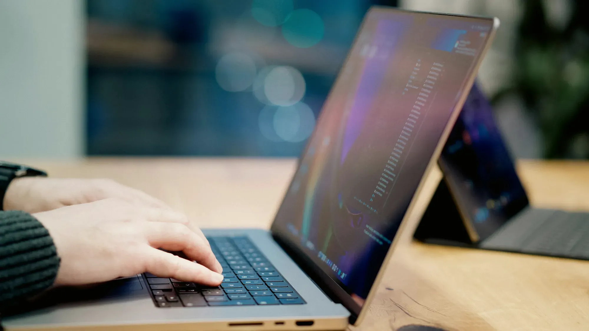 Dłonie na klawiaturze laptopa, w tle drugi ekran