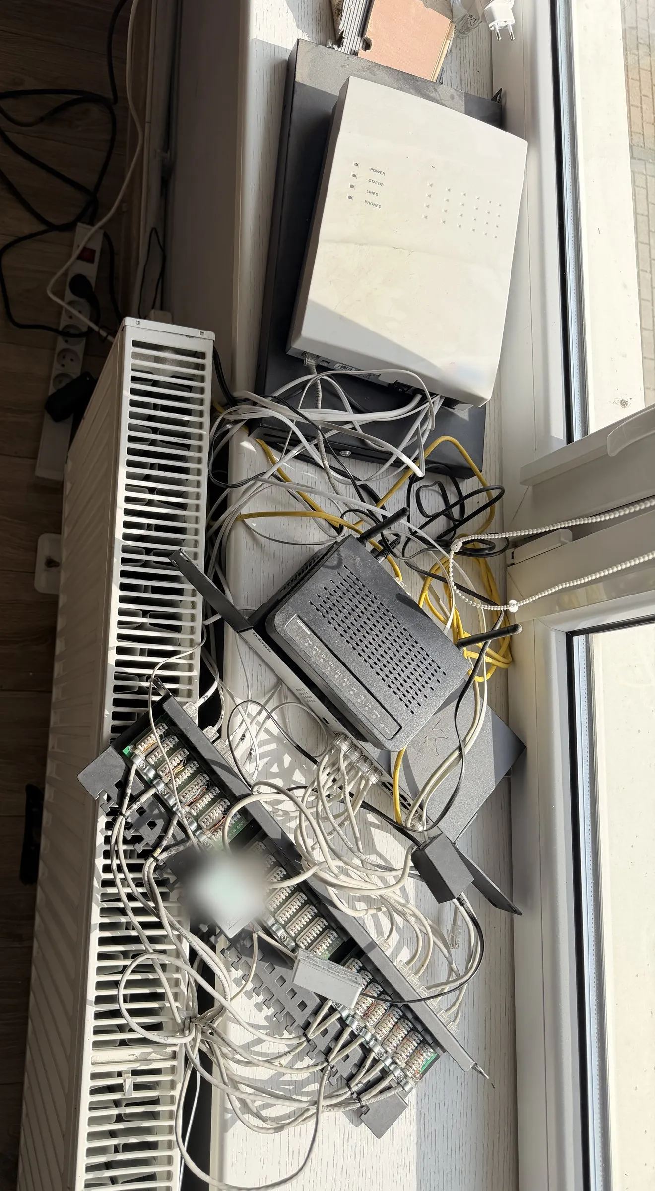 Router, switch, phone system and tangled cables on a windowsill above a radiator