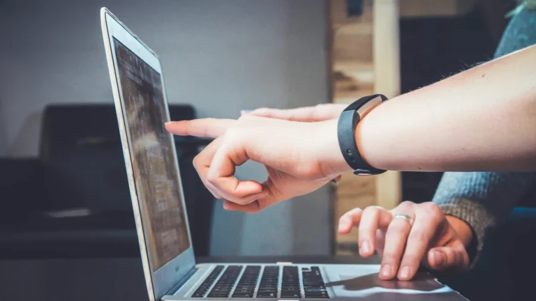 Dłonie wskazujące treść na ekranie laptopa podczas wspólnej pracy przy biurku