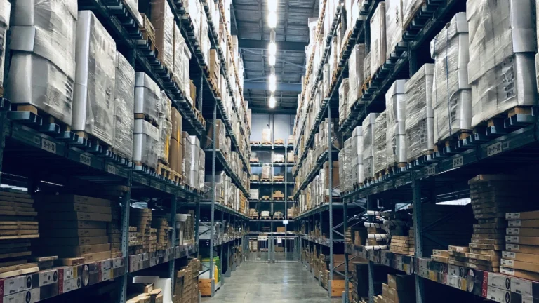 Wąska alejka między wysokimi regałami magazynowymi wypełnionymi paletami